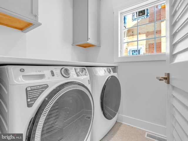 clothes washing area with cabinets and washing machine and clothes dryer