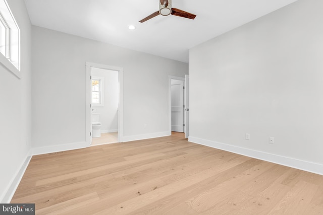 unfurnished bedroom featuring ensuite bath, ceiling fan, multiple windows, and light wood-type flooring