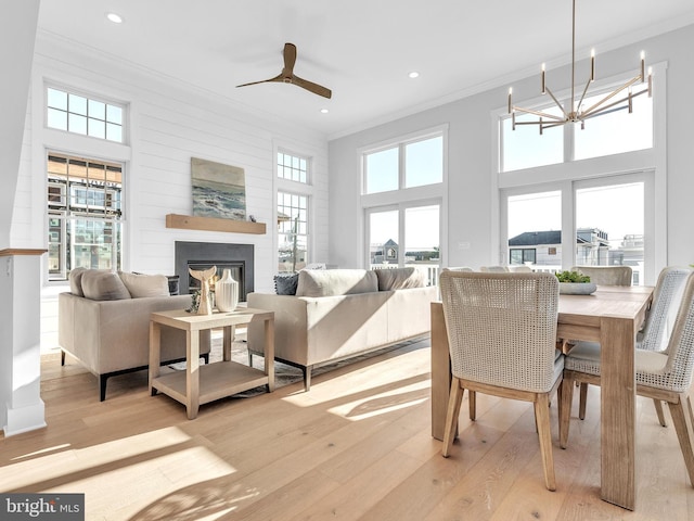 living room with a high ceiling, a large fireplace, light hardwood / wood-style floors, and ceiling fan with notable chandelier