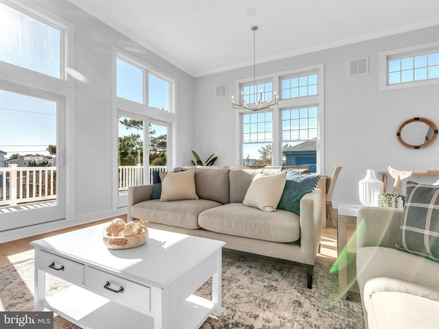 living room featuring light hardwood / wood-style flooring, a healthy amount of sunlight, a notable chandelier, and ornamental molding