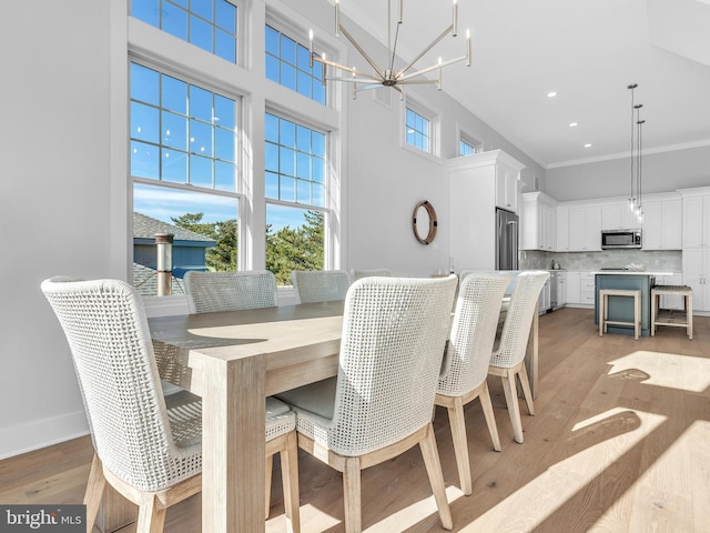 dining room with light wood-type flooring, crown molding, a high ceiling, and an inviting chandelier