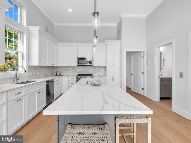 kitchen with pendant lighting, a center island, white cabinets, appliances with stainless steel finishes, and light stone counters