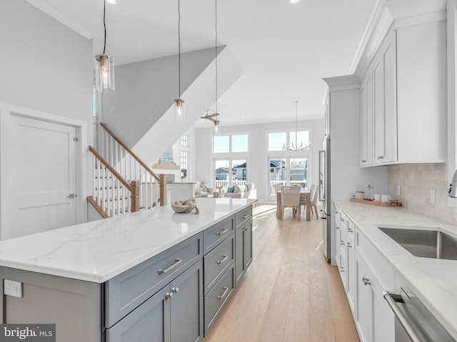 kitchen with tasteful backsplash, light stone counters, sink, decorative light fixtures, and gray cabinets