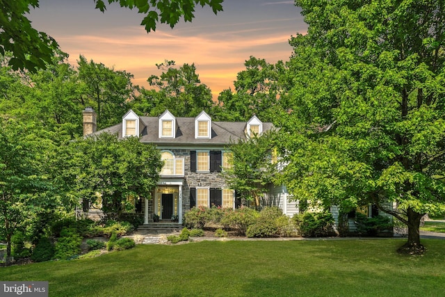 colonial inspired home featuring stone siding and a lawn