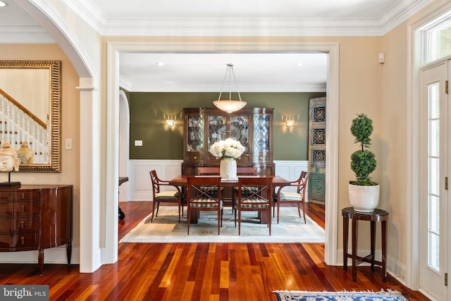 dining room with a wainscoted wall, ornamental molding, wood finished floors, arched walkways, and a decorative wall