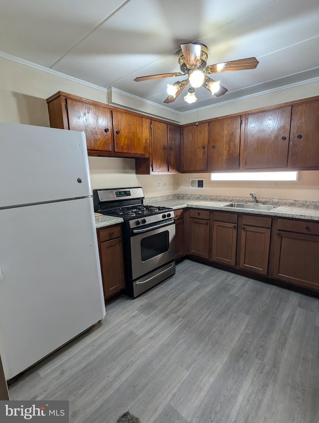 kitchen with stainless steel gas range oven, white fridge, ceiling fan, light hardwood / wood-style floors, and sink