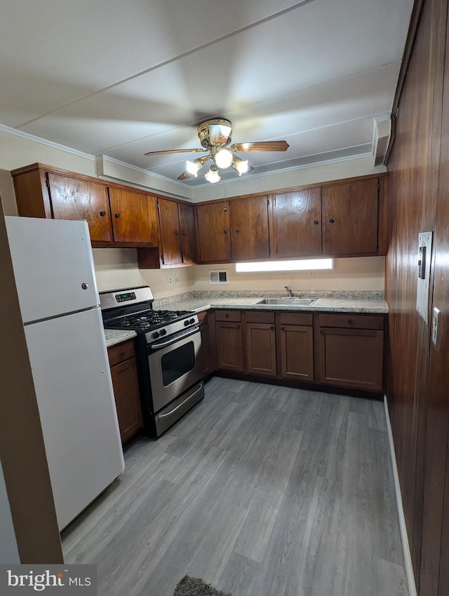 kitchen with white refrigerator, ceiling fan, stainless steel gas range oven, sink, and light hardwood / wood-style flooring