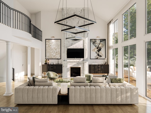 living room featuring high vaulted ceiling, decorative columns, a high end fireplace, and wood-type flooring