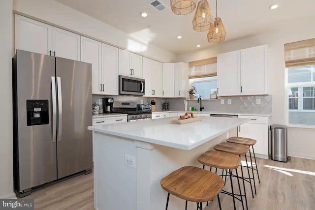 kitchen featuring a kitchen bar, white cabinetry, a center island, hanging light fixtures, and stainless steel appliances