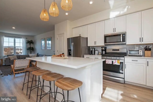 kitchen with a breakfast bar area, white cabinetry, hanging light fixtures, stainless steel appliances, and a kitchen island