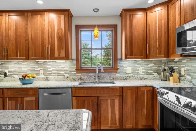 kitchen featuring tasteful backsplash, stainless steel appliances, light stone countertops, sink, and decorative light fixtures