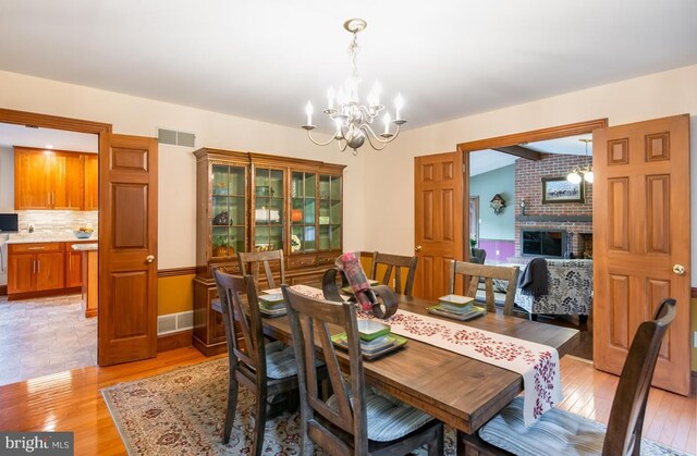 dining area featuring a notable chandelier, a fireplace, light hardwood / wood-style floors, and brick wall