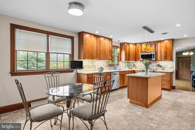 kitchen with light tile patterned floors, appliances with stainless steel finishes, a kitchen island, tasteful backsplash, and decorative light fixtures