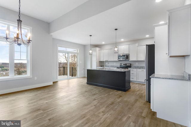 kitchen with appliances with stainless steel finishes, white cabinetry, an island with sink, sink, and hanging light fixtures