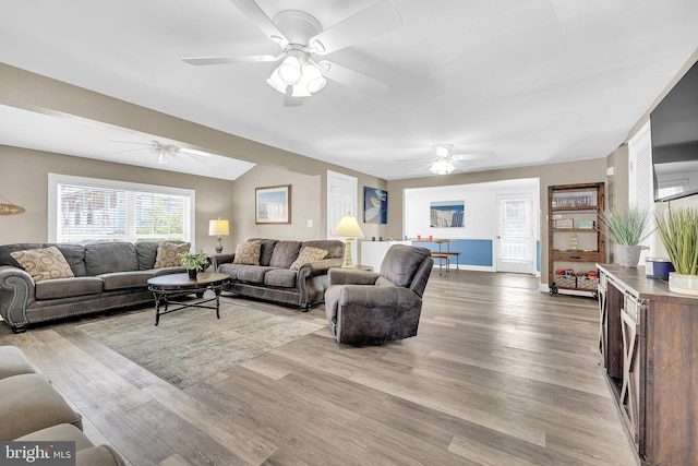 living area featuring ceiling fan, light wood finished floors, vaulted ceiling, and baseboards