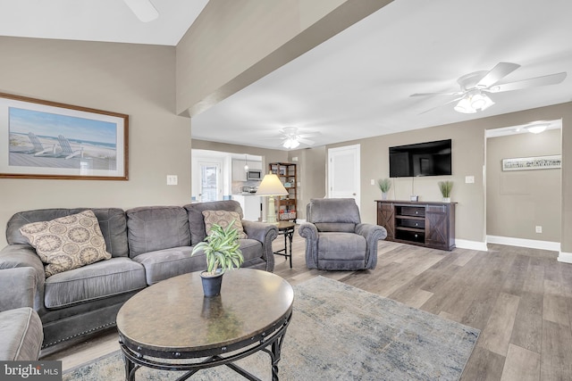 living room featuring light wood-type flooring, baseboards, and a ceiling fan