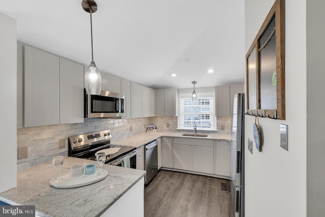 kitchen featuring sink, hanging light fixtures, light stone countertops, light hardwood / wood-style floors, and stainless steel appliances