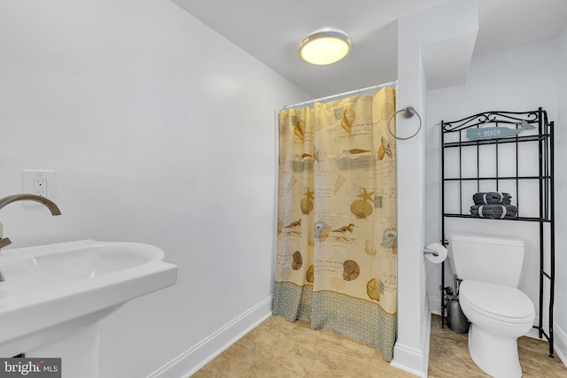 bathroom with a shower with shower curtain, baseboards, a sink, and toilet