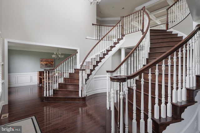 stairs with a decorative wall, wood finished floors, an inviting chandelier, and ornamental molding