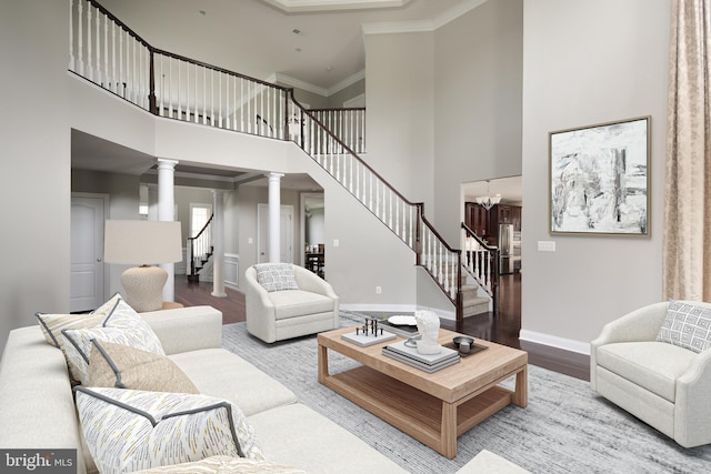 living room featuring wood finished floors, baseboards, ornate columns, ornamental molding, and stairs