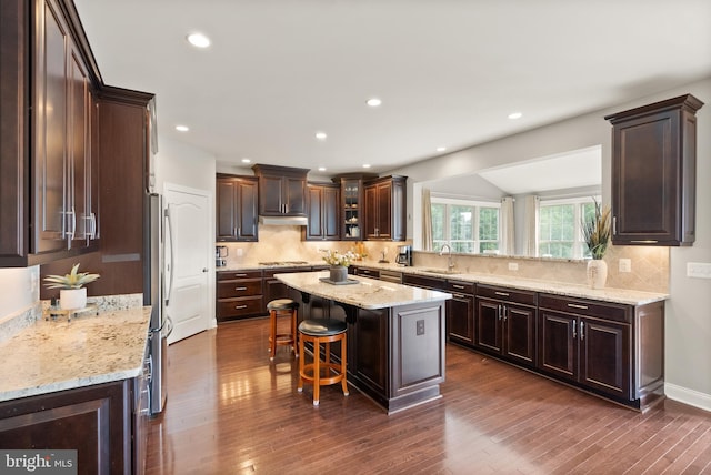 kitchen with dark wood-style floors, a breakfast bar, a sink, dark brown cabinets, and a center island