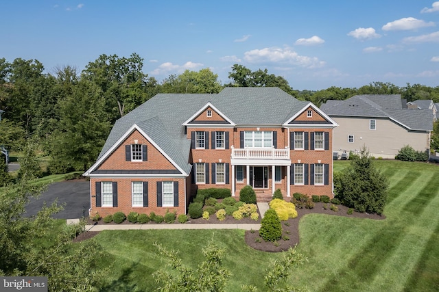 colonial house featuring aphalt driveway, brick siding, and a front yard