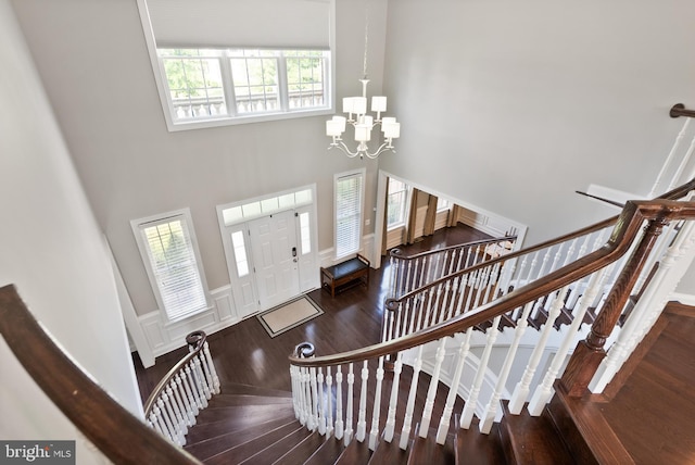 entrance foyer with a chandelier, stairway, wainscoting, a towering ceiling, and wood finished floors