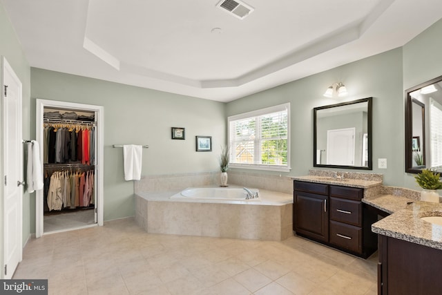 full bathroom with two vanities, a tray ceiling, a garden tub, and visible vents