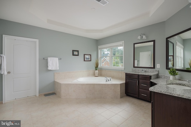 full bath featuring a garden tub, two vanities, a tray ceiling, tile patterned floors, and a sink