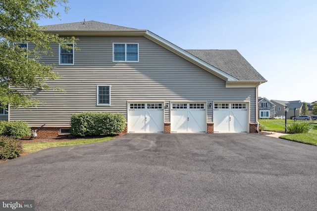 view of home's exterior featuring a garage, roof with shingles, and driveway