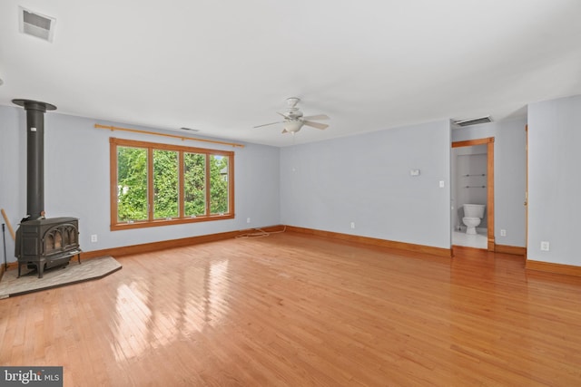 unfurnished living room featuring ceiling fan, light hardwood / wood-style flooring, and a wood stove