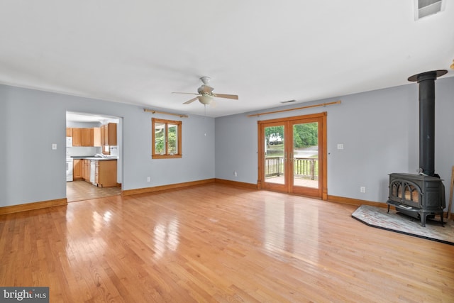 unfurnished living room featuring a wealth of natural light, ceiling fan, light tile patterned flooring, and a wood stove