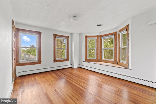 spare room featuring a wealth of natural light, hardwood / wood-style floors, and a baseboard heating unit