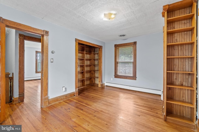 unfurnished bedroom with a closet, a textured ceiling, baseboard heating, and light hardwood / wood-style floors