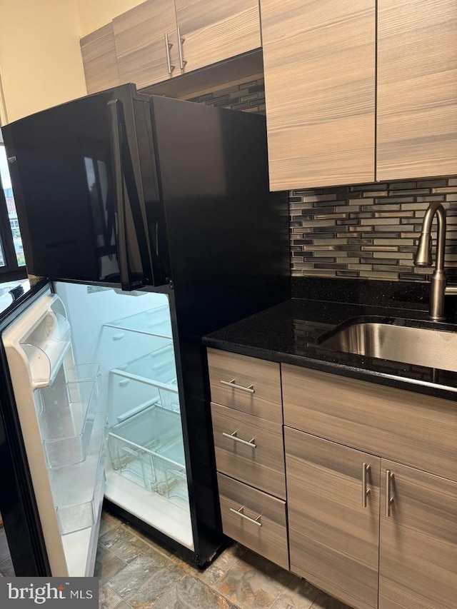 kitchen featuring black refrigerator, sink, decorative backsplash, and dark stone counters