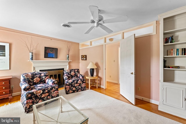 sitting room featuring built in shelves, light hardwood / wood-style flooring, and ceiling fan