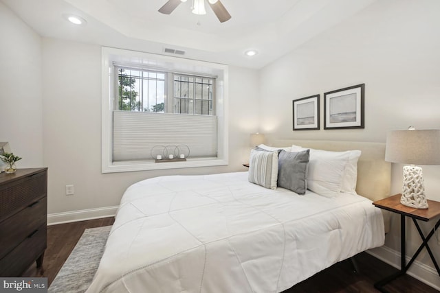 bedroom with ceiling fan, dark hardwood / wood-style flooring, and a tray ceiling