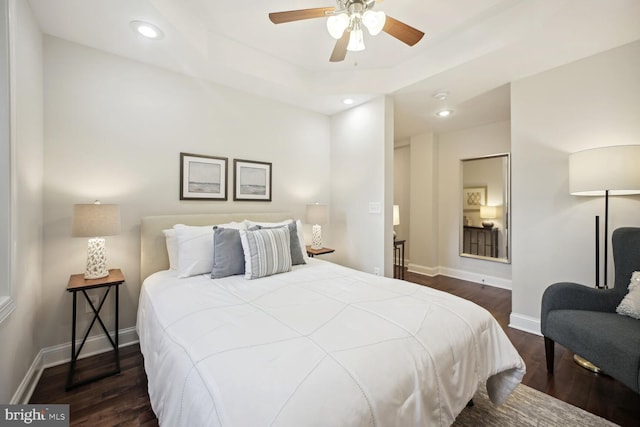 bedroom featuring dark hardwood / wood-style floors, ceiling fan, and a tray ceiling