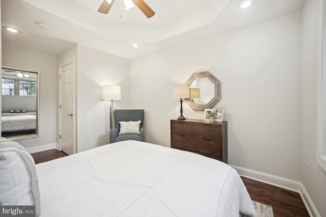 bedroom with ceiling fan, a tray ceiling, and dark hardwood / wood-style flooring