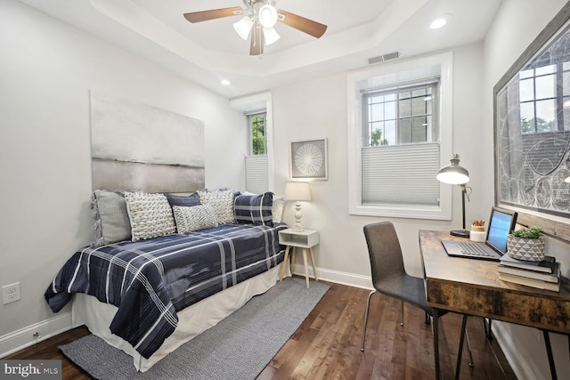 bedroom with multiple windows, dark wood-type flooring, and a tray ceiling