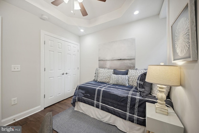 bedroom with dark hardwood / wood-style flooring, a closet, a raised ceiling, and ceiling fan