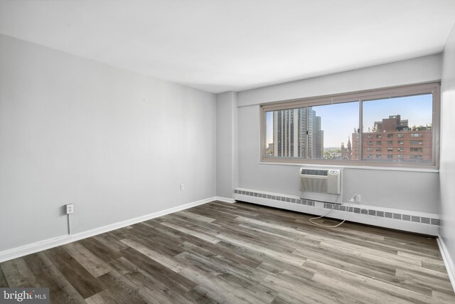 empty room featuring a wall mounted AC, wood-type flooring, and baseboard heating