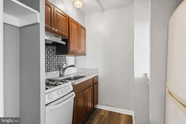 kitchen featuring dark hardwood / wood-style flooring, white appliances, sink, light stone countertops, and backsplash