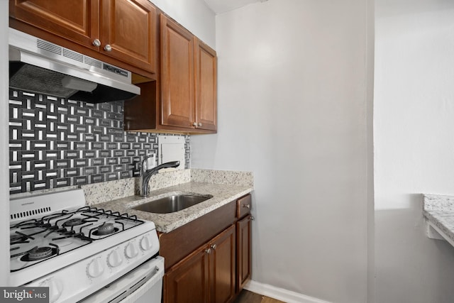 kitchen featuring backsplash, white range oven, light stone countertops, hardwood / wood-style flooring, and sink