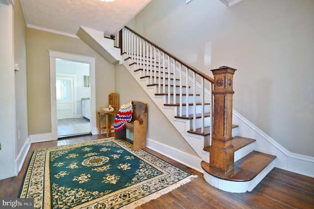 staircase featuring wood-type flooring, ornamental molding, and a textured ceiling