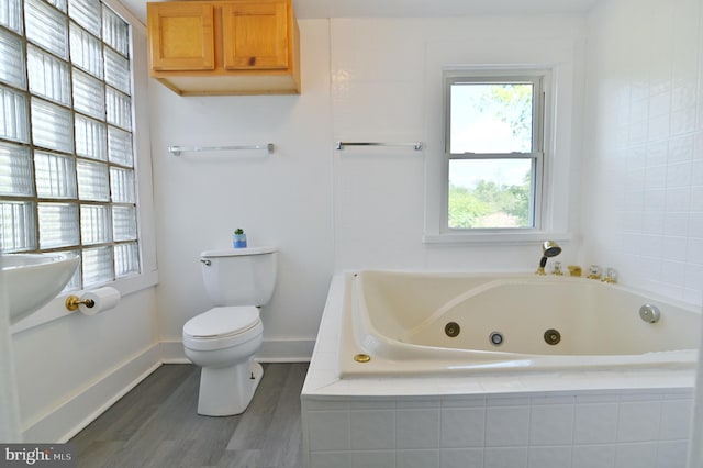 bathroom featuring wood-type flooring, tiled bath, and toilet