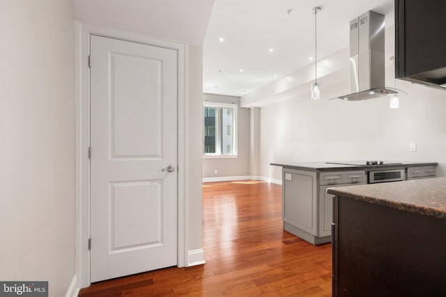 kitchen with wall chimney range hood, black electric stovetop, hanging light fixtures, hardwood / wood-style flooring, and kitchen peninsula