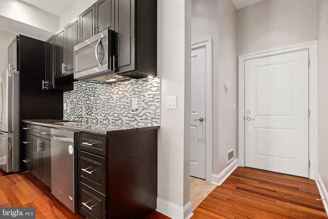 kitchen featuring a sink, wood finished floors, appliances with stainless steel finishes, tasteful backsplash, and dark stone countertops