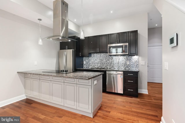 kitchen featuring tasteful backsplash, island range hood, dark stone counters, appliances with stainless steel finishes, and a peninsula