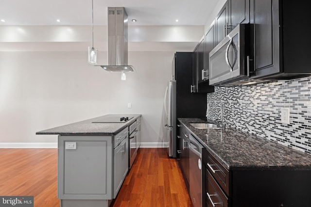 kitchen featuring stainless steel appliances, a sink, dark stone counters, island exhaust hood, and decorative light fixtures